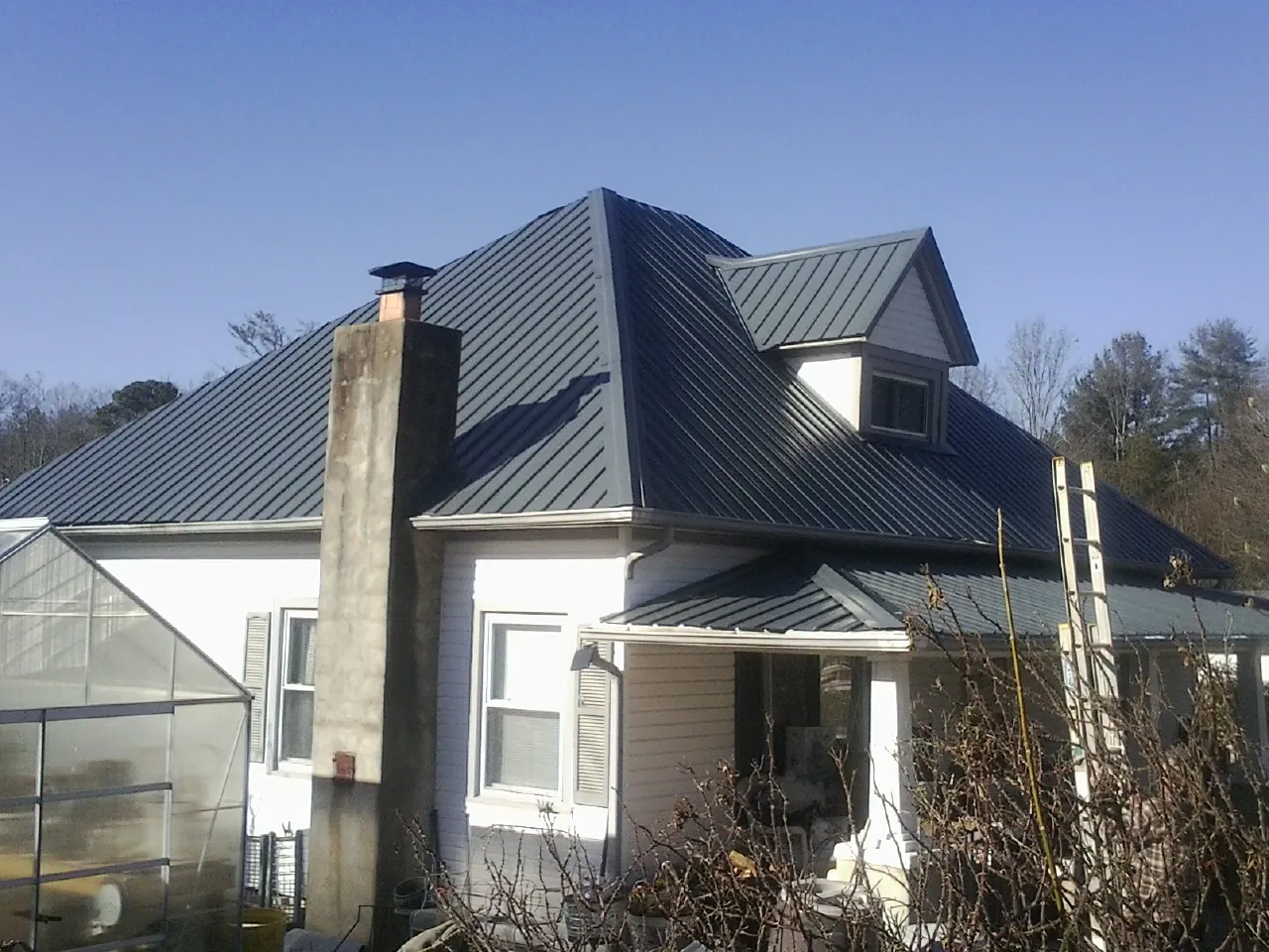 Dark blue standing seam metal roof on a white farmhouse with dormer — Slate & Tile Roof Repair by Roofing Brothers in Minden