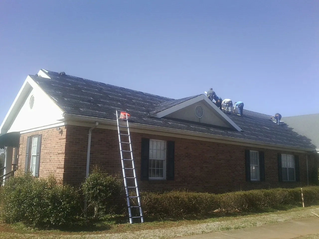 Crew tearing shingles off a brick ranch roof with a ladder set — Emergency Roof Repair work by our crew in Minden