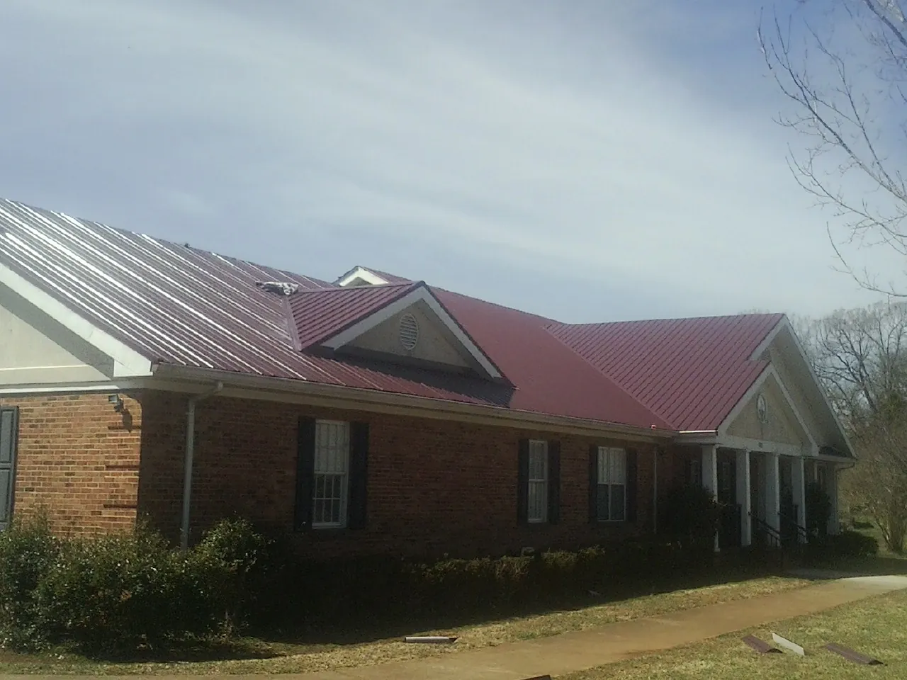 Red metal roof with gabled entries on a long brick building, from a Hail Damage Roof Repair job in Minden